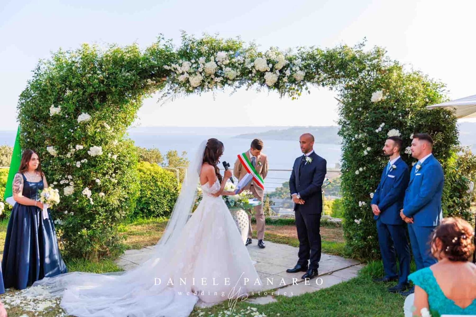 Gli sposi durante la cerimonia civile sotto l’arco di verde e rose bianche affacciato sul mare — Cala dei Balcani, Santa Cesarea Terme, Salento