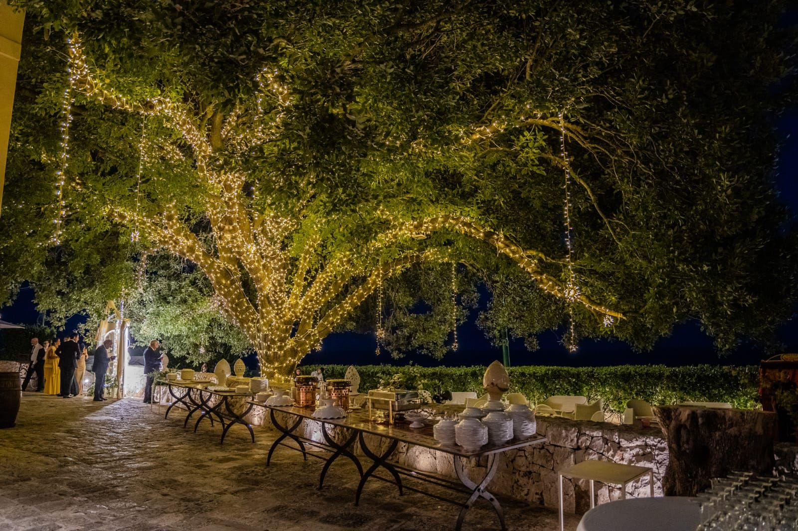 Il Giardino della Quercia illuminato di sera con i tavoli del buffet del ricevimento &mdash; Cala dei Balcani, Santa Cesarea Terme, Salento