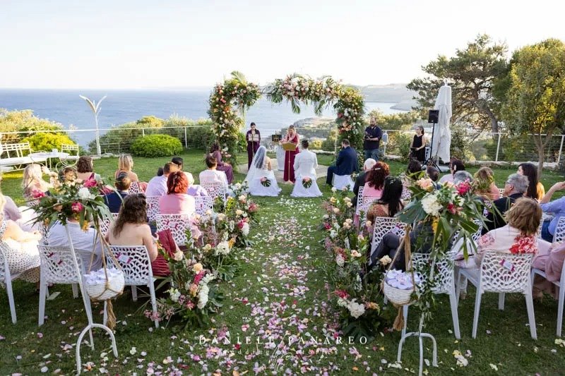 Ceremonia al aire libre con arco de flores rosas y pétalos sobre el césped — boda de destino internacional en Cala dei Balcani, Salento