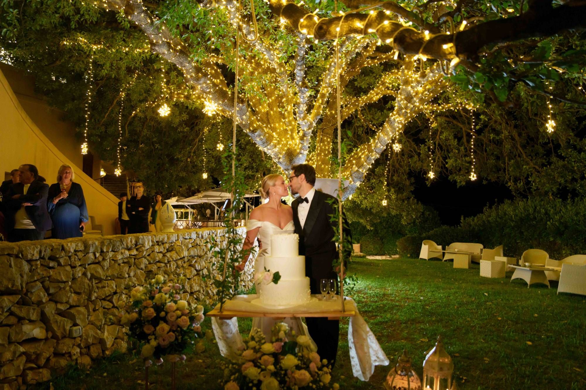 Gli sposi davanti alla torta nuziale sotto la quercia secolare illuminata &mdash; matrimonio a Cala dei Balcani, Santa Cesarea Terme, Salento